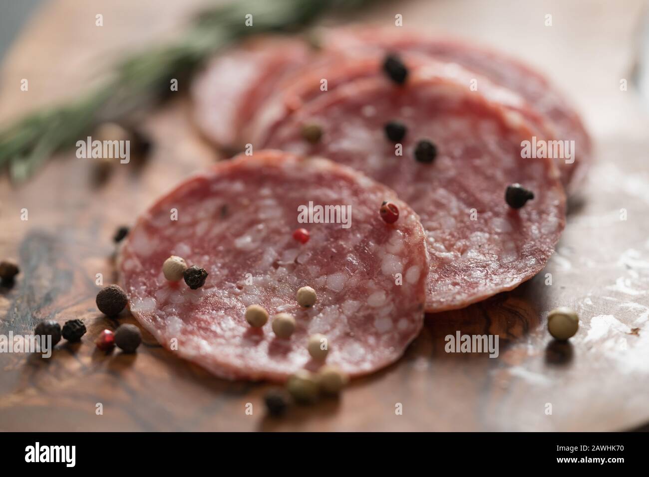 Sliced salame milano sausage on olive wood board with rosemary and pepper, shallow focus Stock Photo