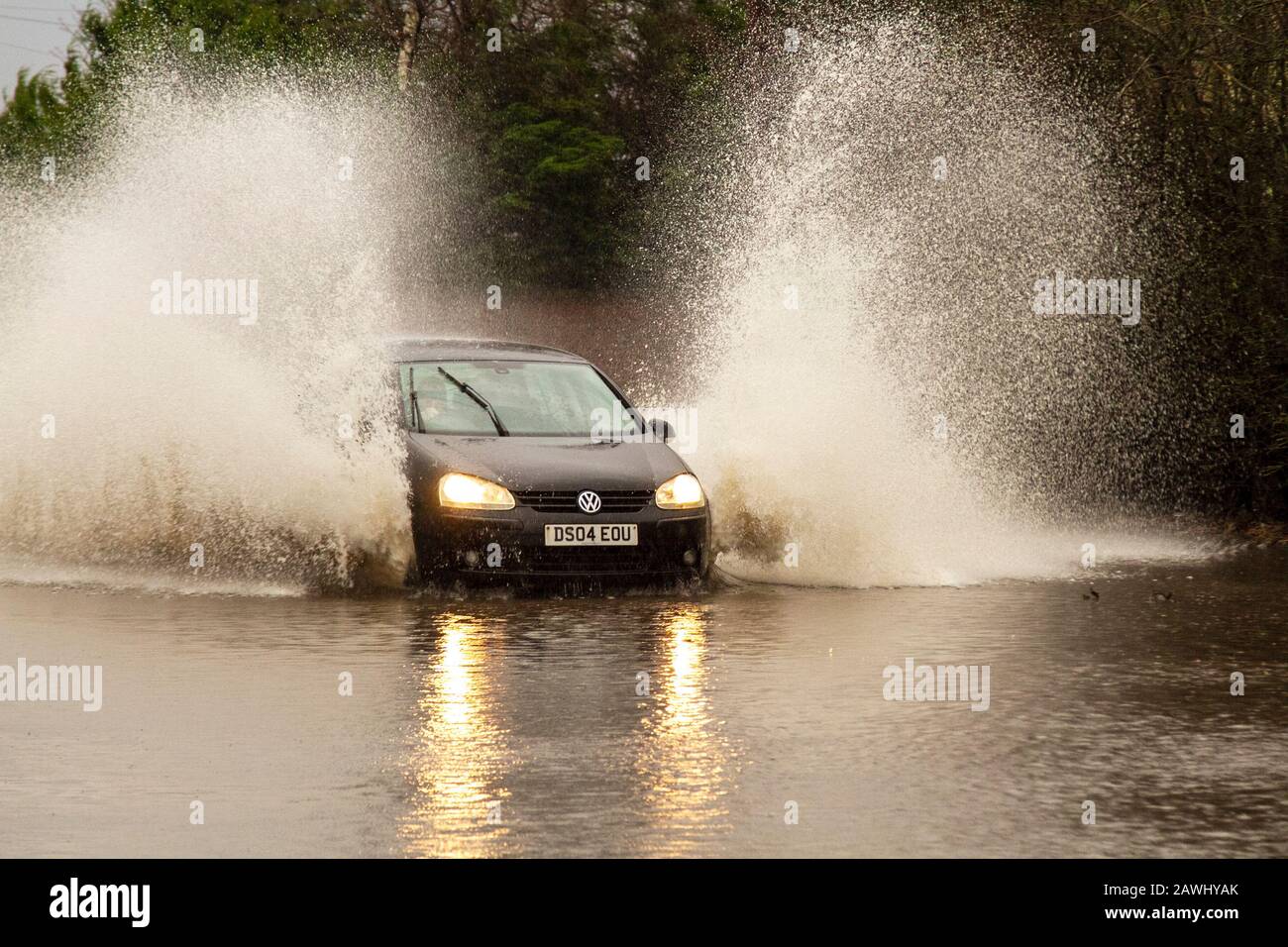 A car passing through deep flood waters at speed throwing up spray on a road in Kirkham