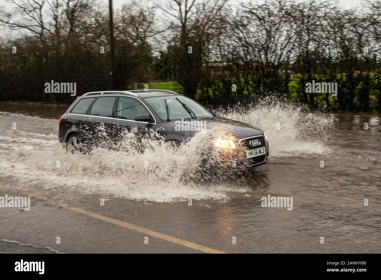 A car passing through deep flood waters at speed throwing up spray on a road in Kirkham