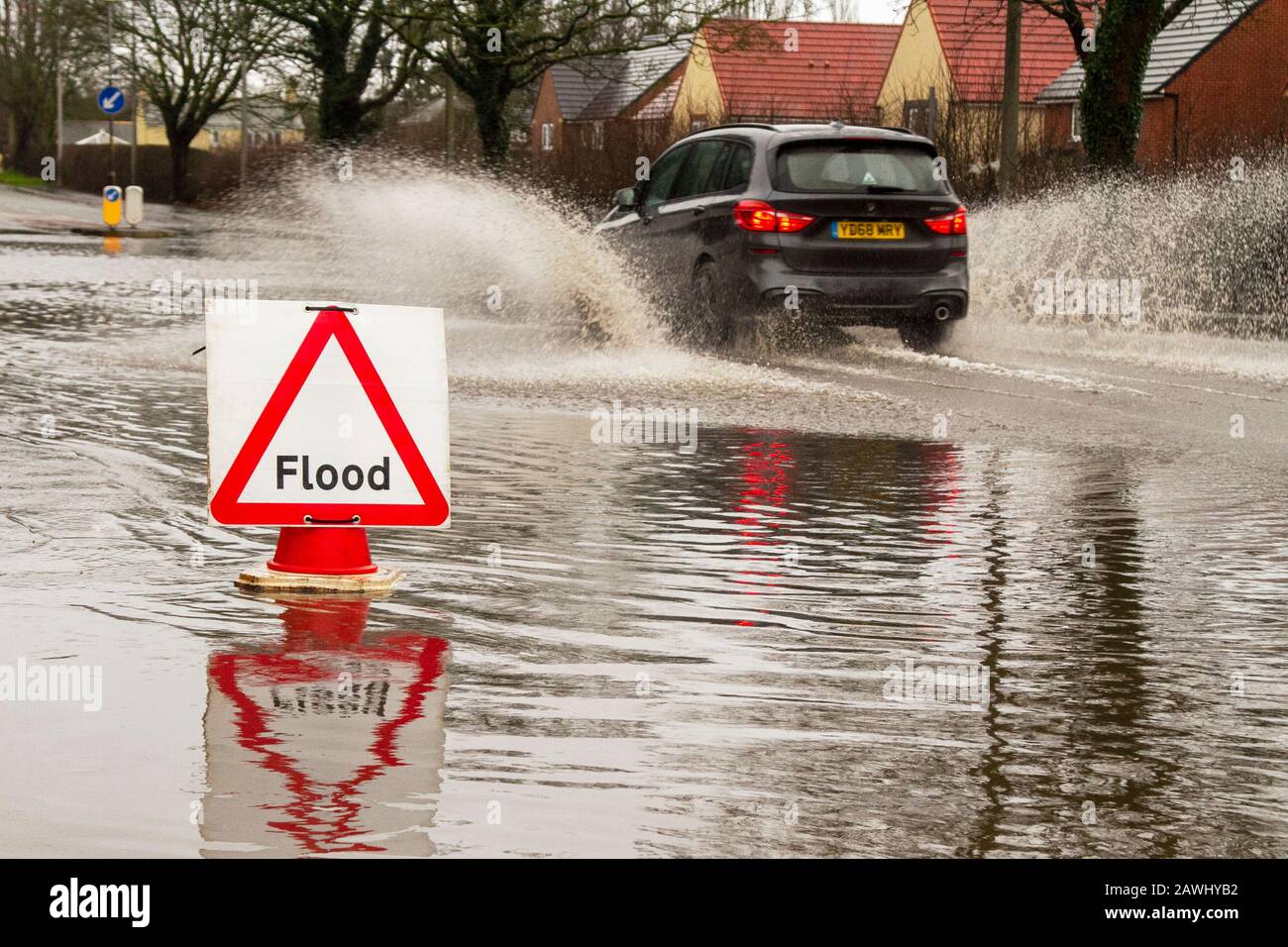 A car passing through deep flood waters at speed throwing up spray on a road in Kirkham