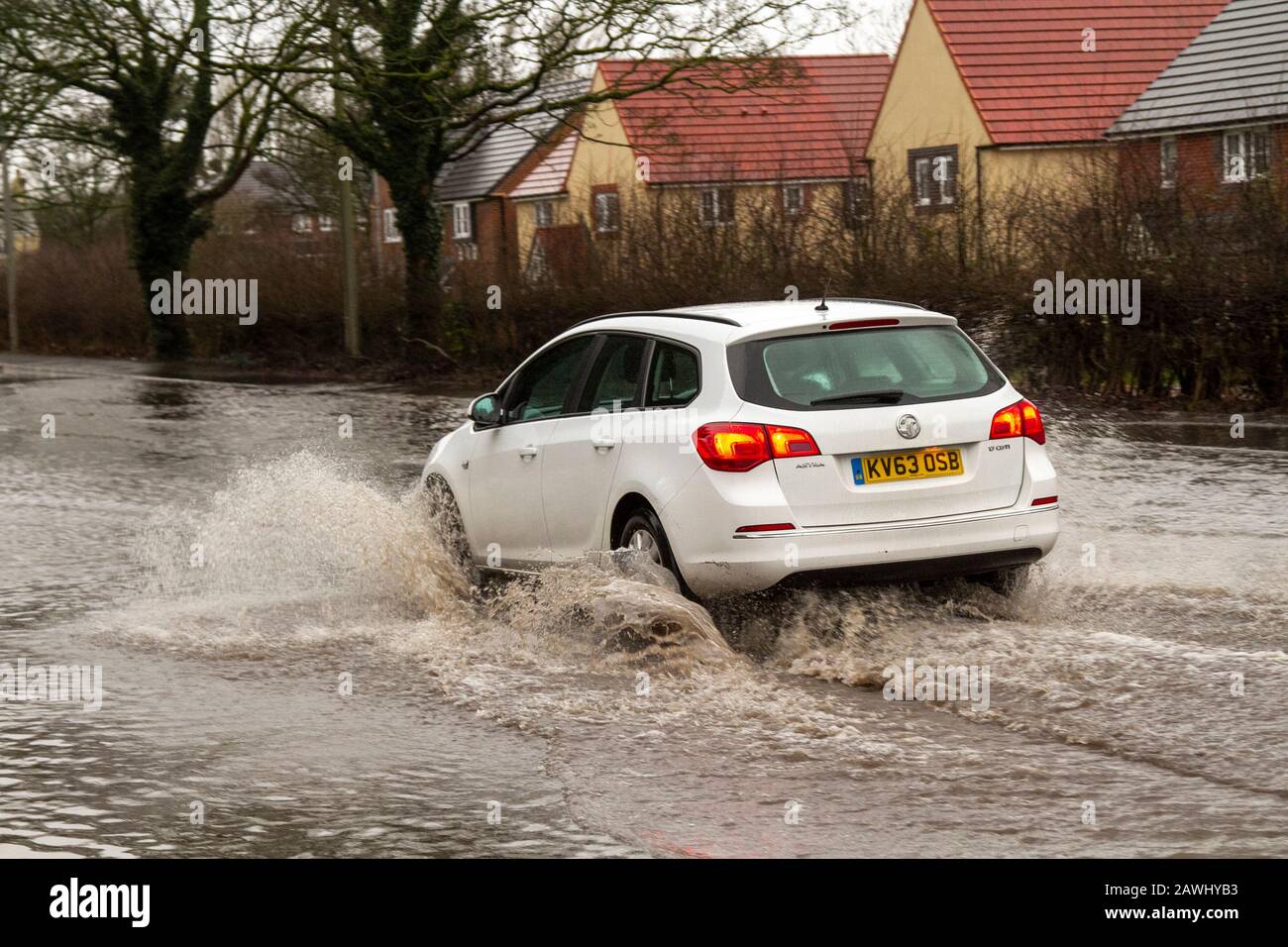 A car passing through deep flood waters at speed throwing up spray on a road in Kirkham