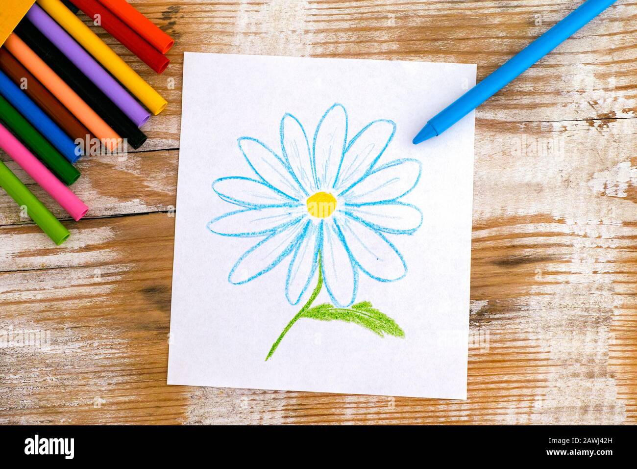 Child hand drawing Daisy Flower with wax crayons. Wooden background