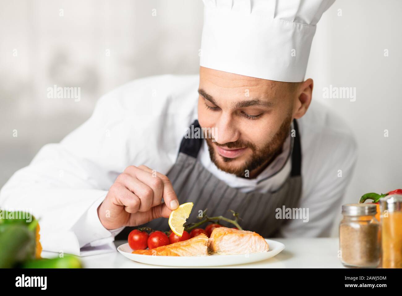 Professional Chef Plating Roasted Salmon Standing In Kitchen Stock Photo
