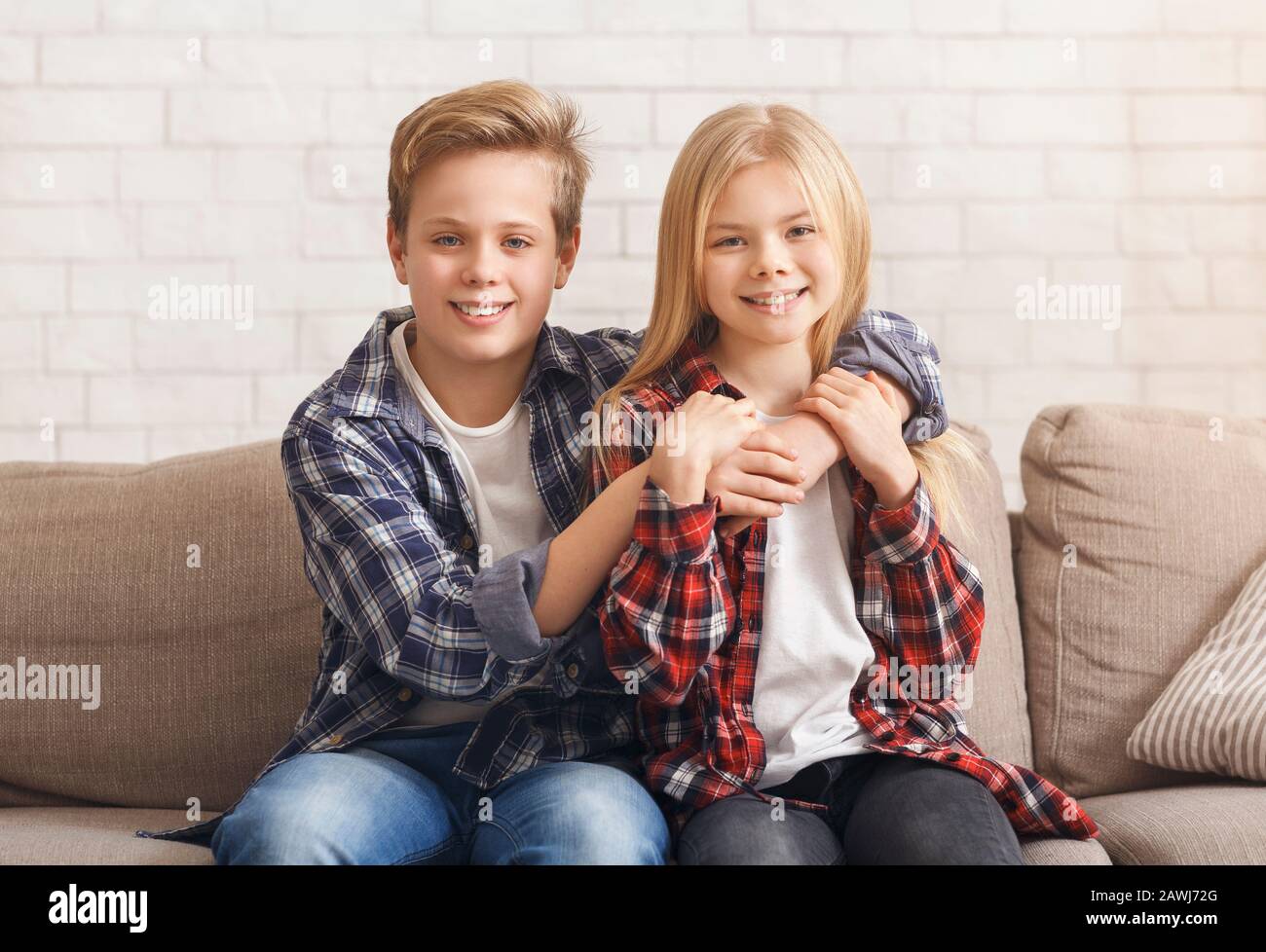 Cute Boy And Girl Hugging Sitting On Sofa At Home Stock Photo