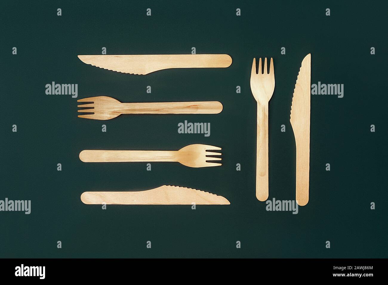 Set of disposable wooden knives and forks on a dark green emerald