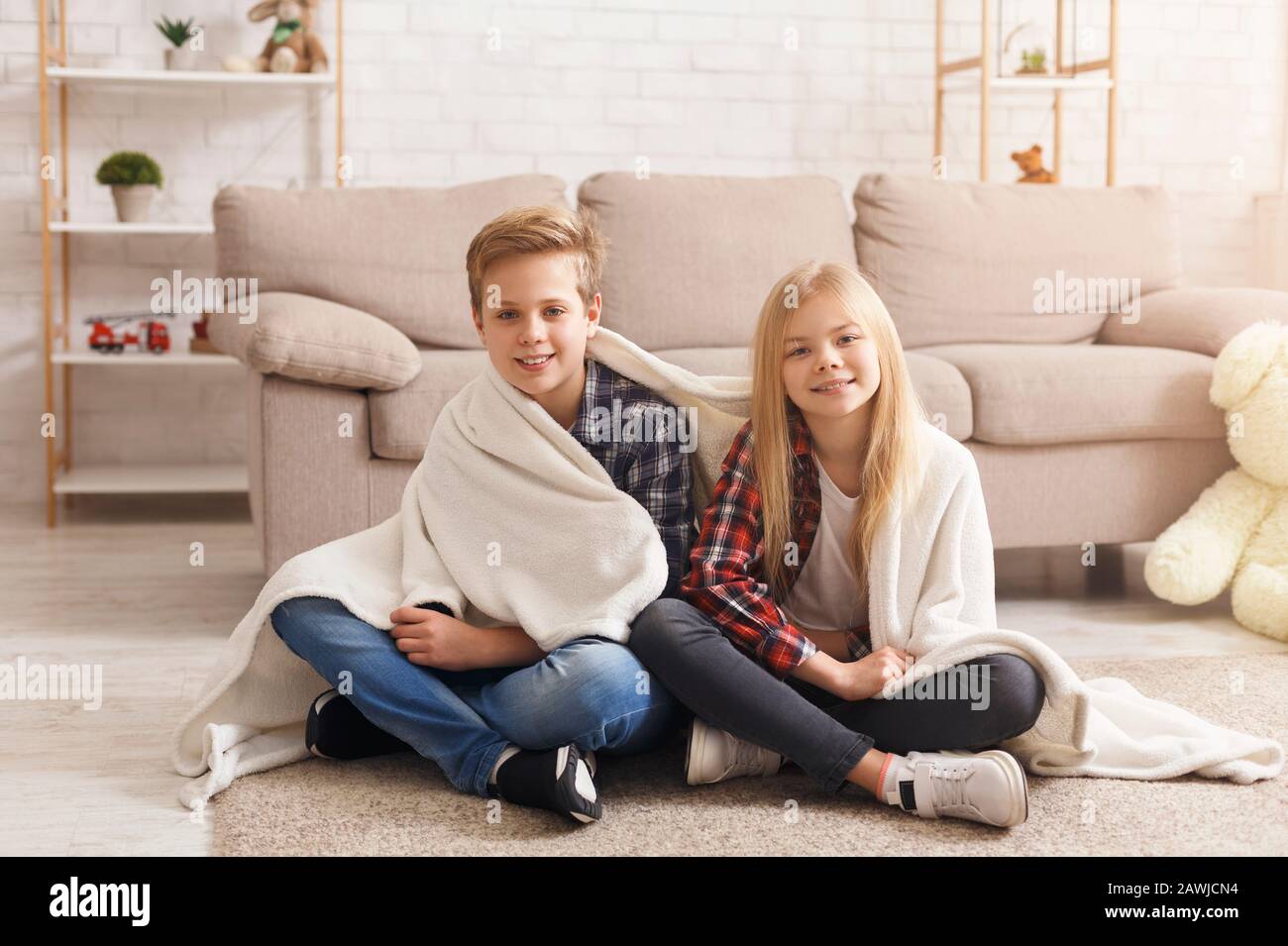 Cute Brother And Sister Covered With Blanket Sitting On Floor Stock Photo