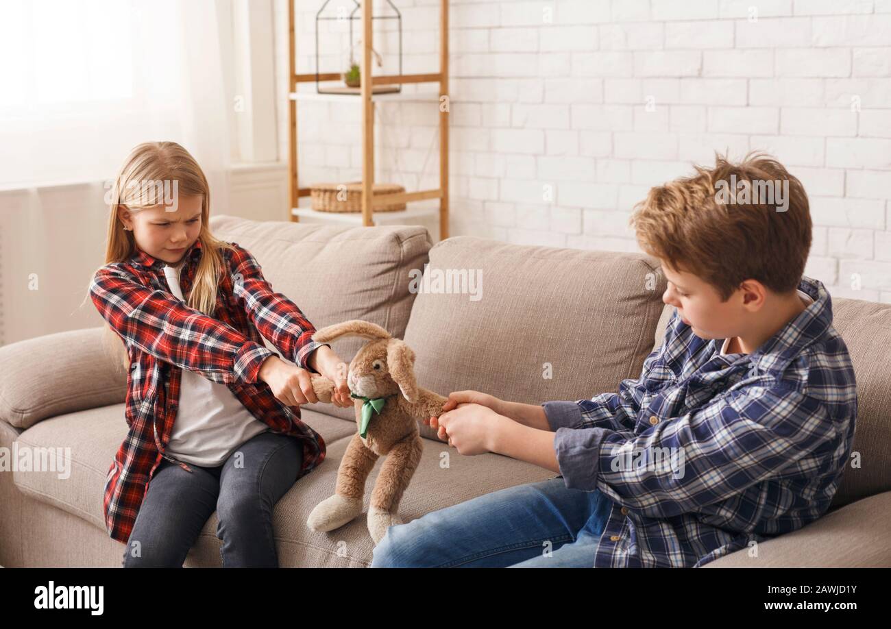Greedy Brother And Sister Pulling Apart Toy Sitting On Sofa Stock Photo