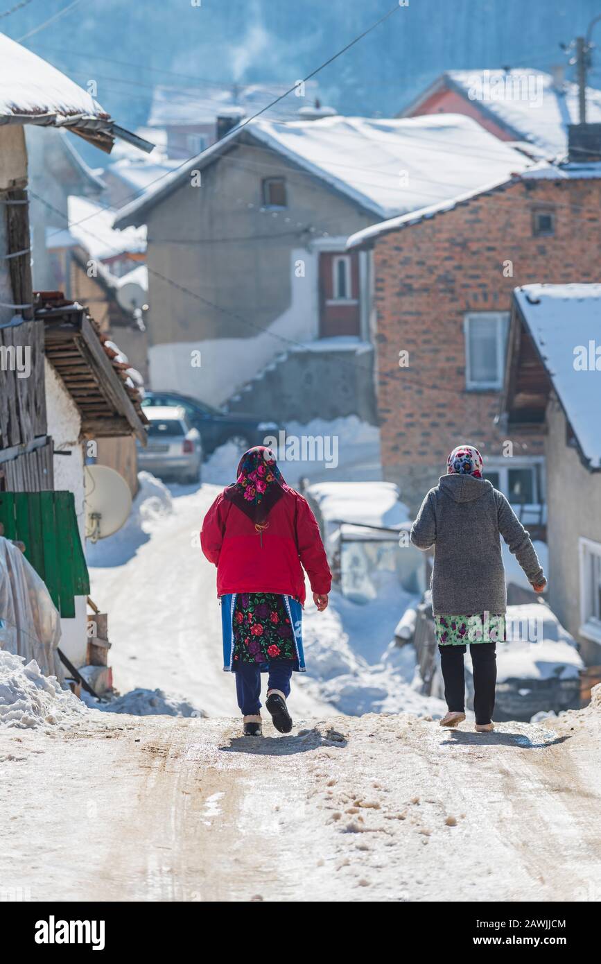 Grashevo village, Rhodope mountains, Bulgaria - 02.08.2020: Old woman walk on snowy road in winter in high mountain village Grashevo in Rhodopes mount Stock Photo