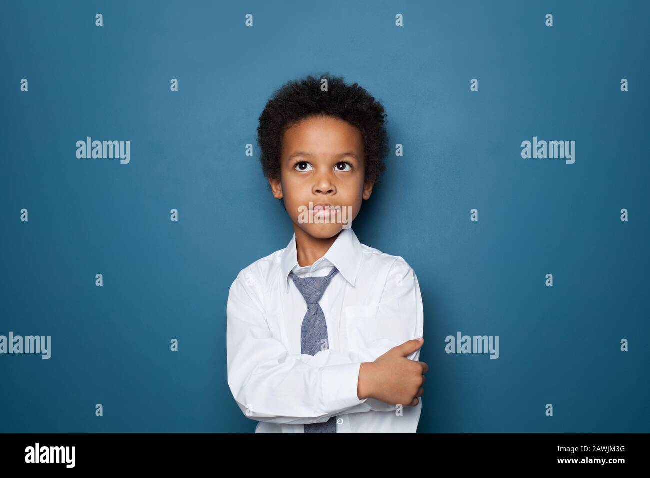 Smart african american kid boy student with crossed arms looking up on blue background. Little black child school boy Stock Photo