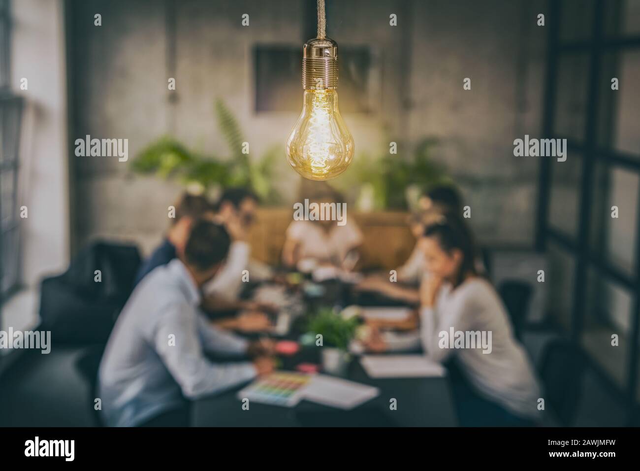 Young business people are discussing together a new startup project. A glowing light bulb as a new idea. Stock Photo