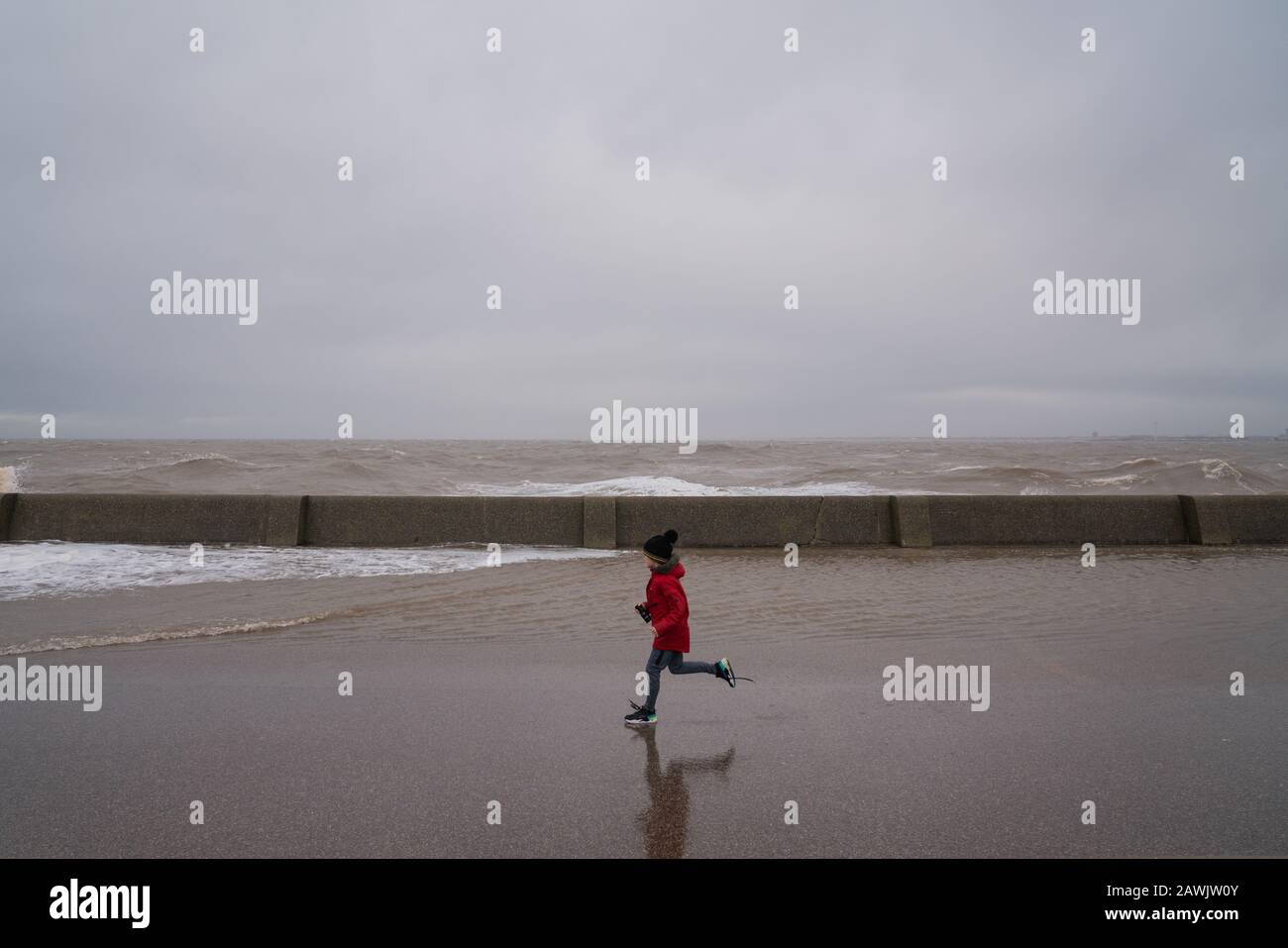 New Brighton, Wirral, UK. 9th Feb, 2020. A child runs along the promenade as gale force winds and waves crashed into the promenade at New Brighton on the Wirral in the north west of England on Sunday, February 9, 2020. Credit: Christopher Middleton/Alamy Live News Stock Photo