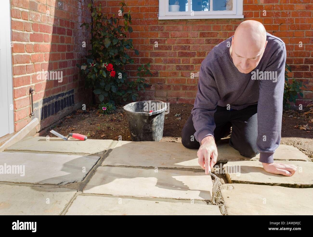 Builder laying and grouting York stone paving slabs outdoors, DIY home patio project , UK Stock Photo