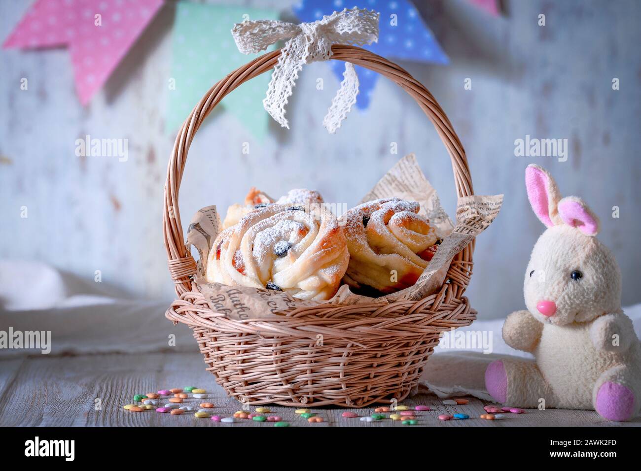 Easter bunny next to a basket filled with pastries. Kruffins with raisins and dried apricots, sprinkled with powdered sugar on top. Festive mood. Stock Photo