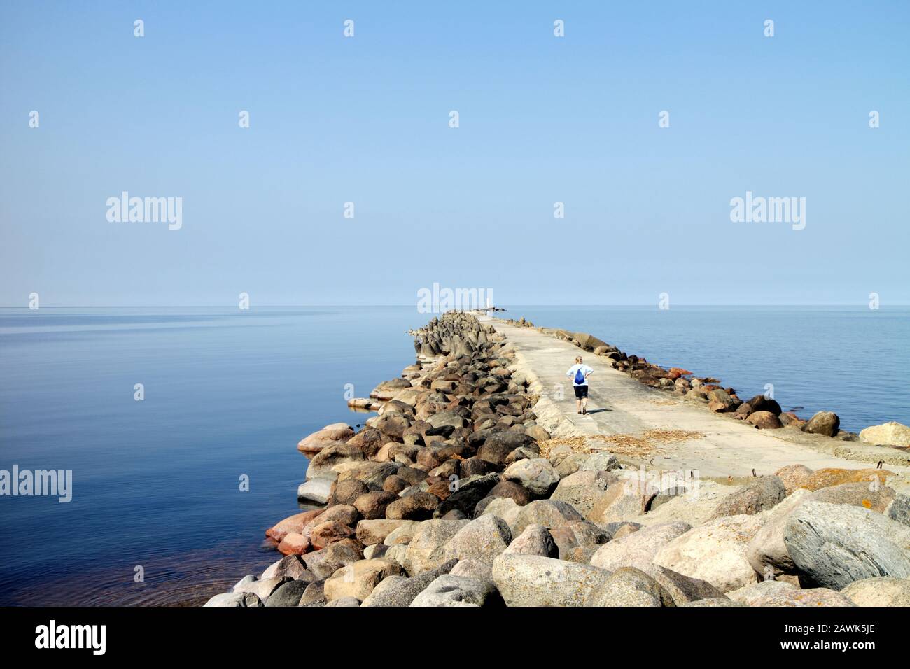 stony pier with a lighthouse on the calm Baltic Sea with one traveler enjoying the summer landscape Stock Photo