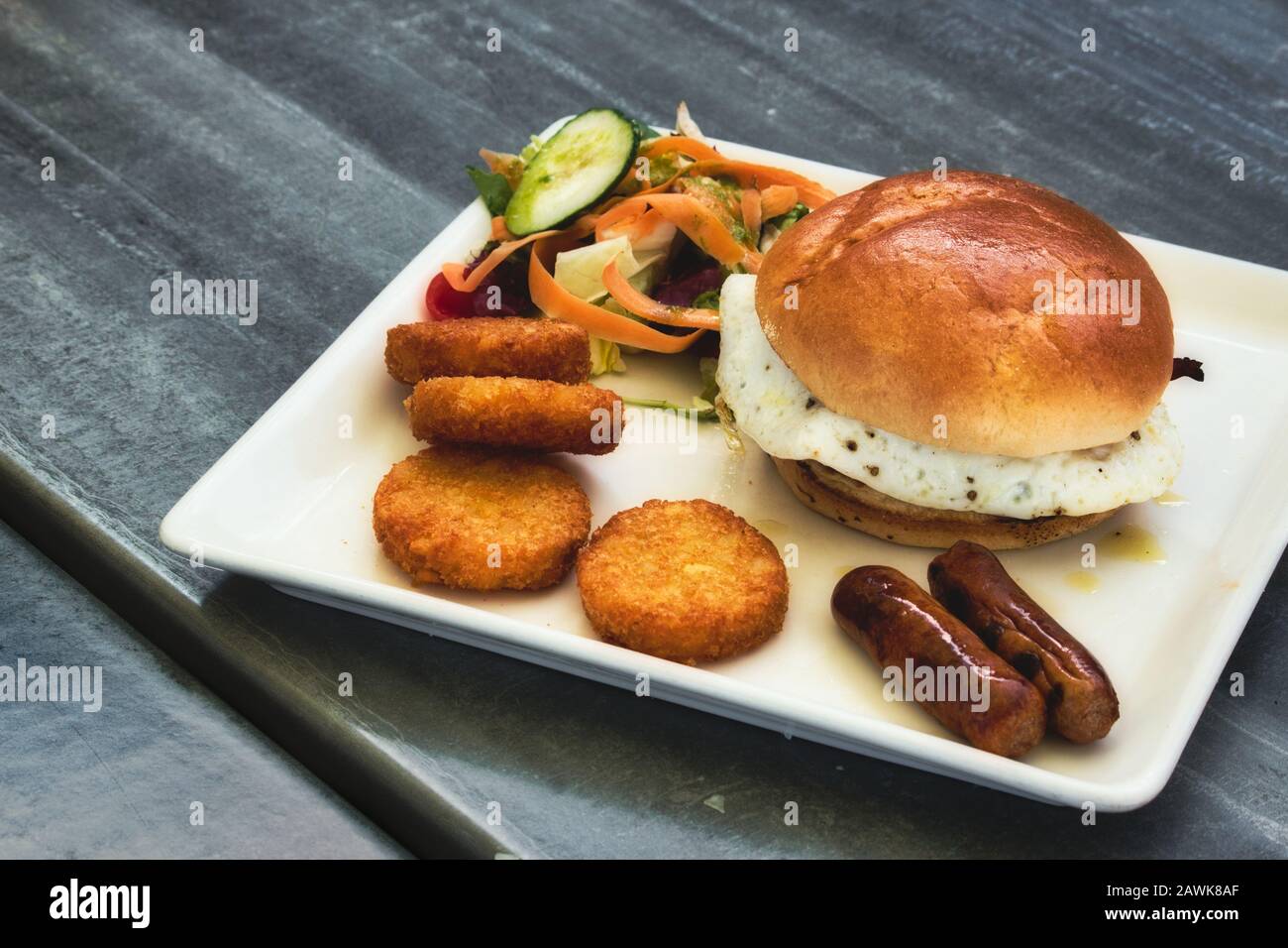 Breakfast brioche with fried egg, sausages, hash browns and salad Stock Photo