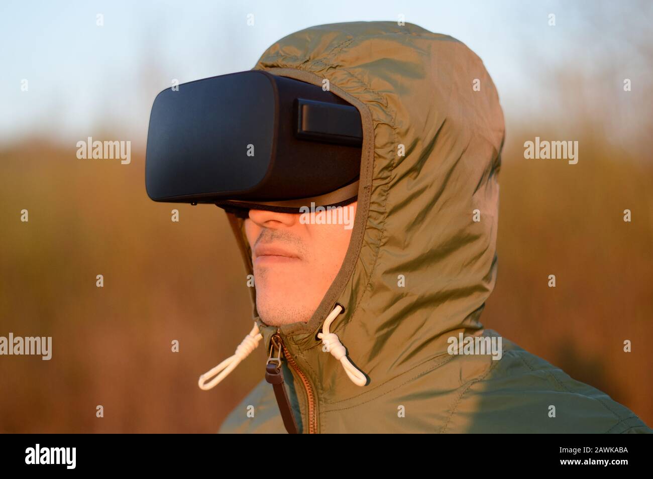 Portrait of a happy young man with virtual reality headset and in a green protective hood outdoors at sunset Stock Photo