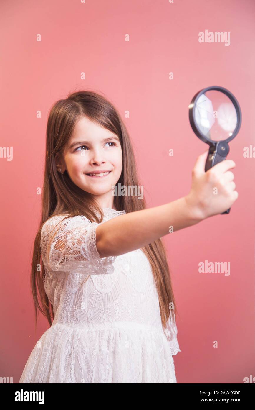 girl plays with a magnifying glass, looking through it at the pink wall Stock Photo