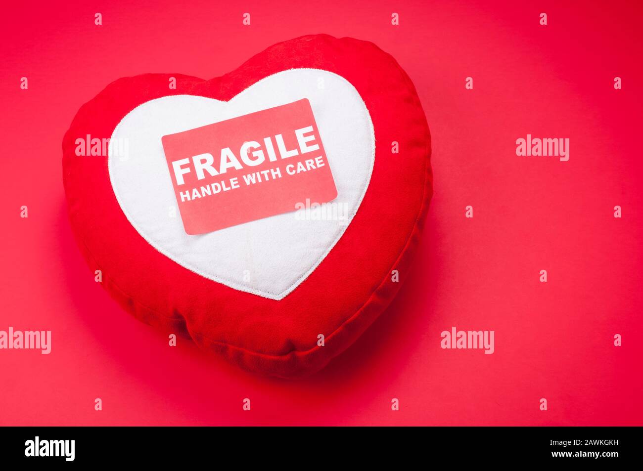 Valentine's Day heart cushion sitting on a bright red background with a Fragile Handle With Care Sticker Stock Photo