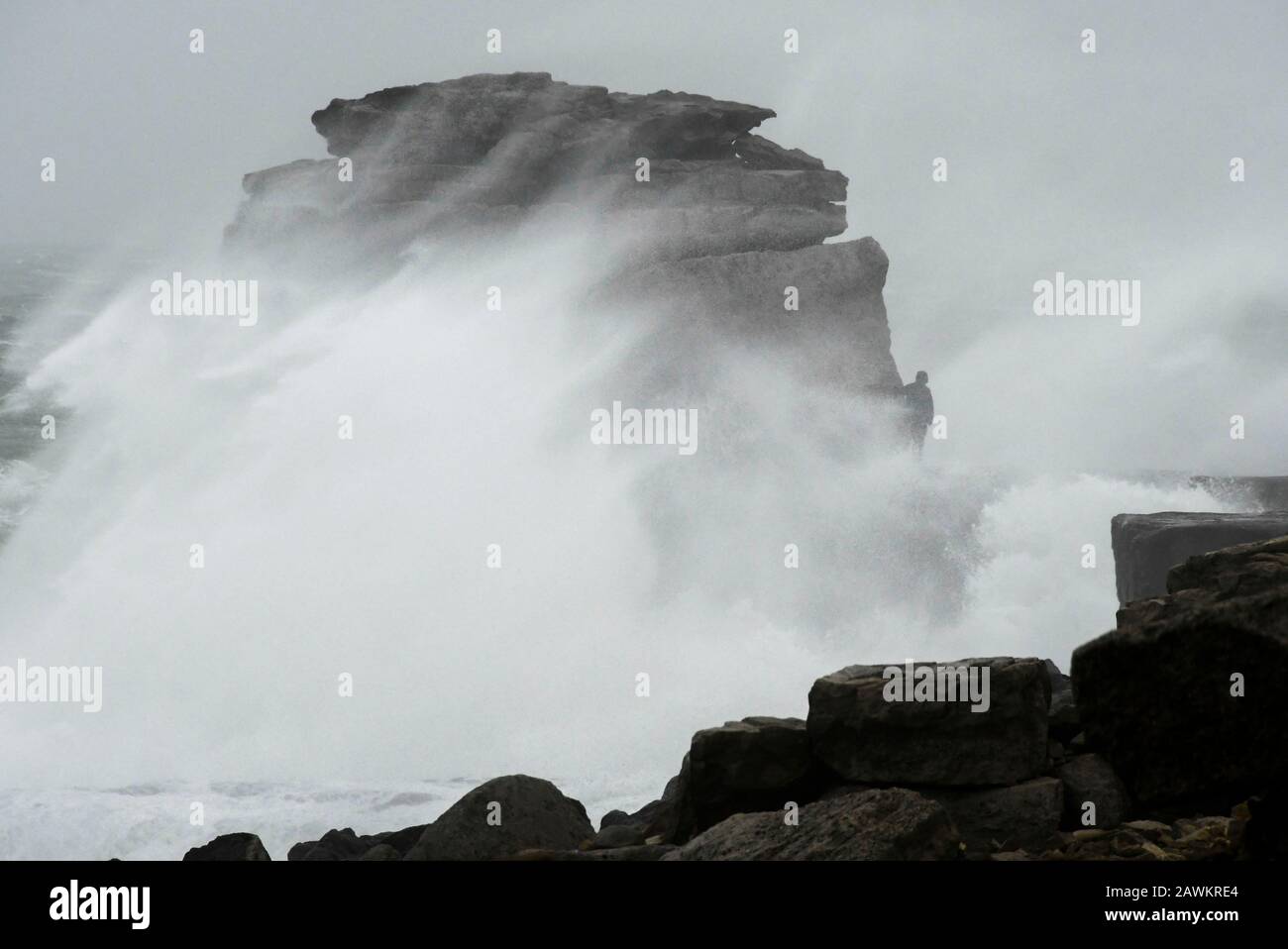 Portland Bill, Dorset, UK.  9th February 2020. UK Weather.  A thrill seeker risks his life by walking onto Pulpit Rock at Portland Bill in Dorset and risks being swept in to the sea as huge waves from Storm Ciara crash against the limestone pillar.  Picture Credit: Graham Hunt/Alamy Live News Stock Photo