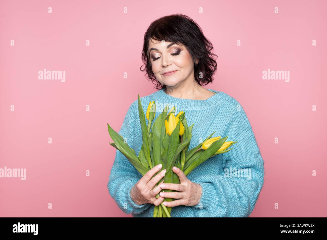 Beautiful old woman with professional smokey make-up and hairstyle holding tulip flowers on the pink background Stock Photo