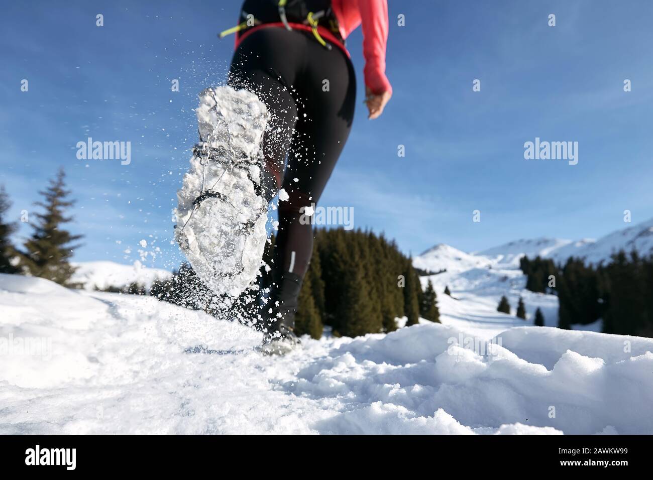 Close-up shoes of trail runner woman running in winter mountains trail on snow.  Stock Photo