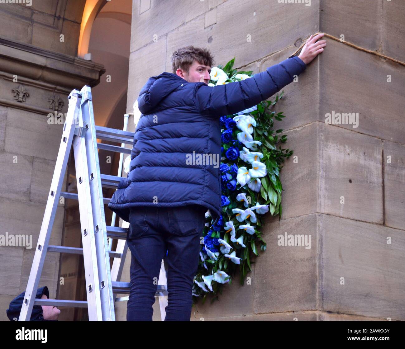 Netflix is filming for series four of The Crown in Manchester, uk. A worker puts up a large flower wreath on the exterior of the Edwardian Hotel on Peter Street in central Manchester to prepare for filming. The Crown is a historical drama web television series about the reign of Queen Elizabeth II. Stock Photo