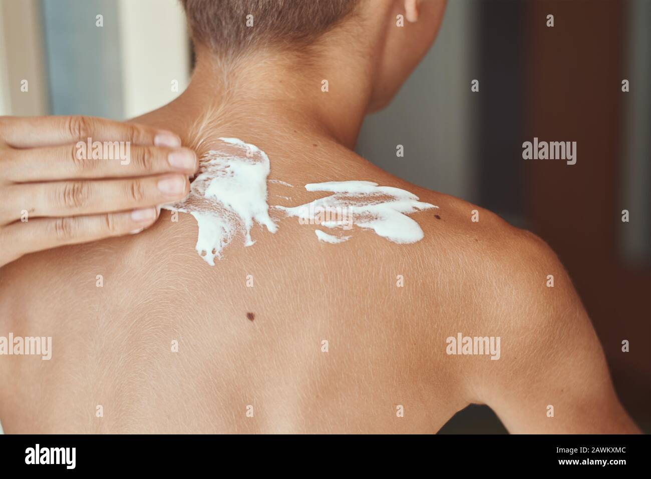 Boy in cozy beige clothes applying sunscreen protection creme on