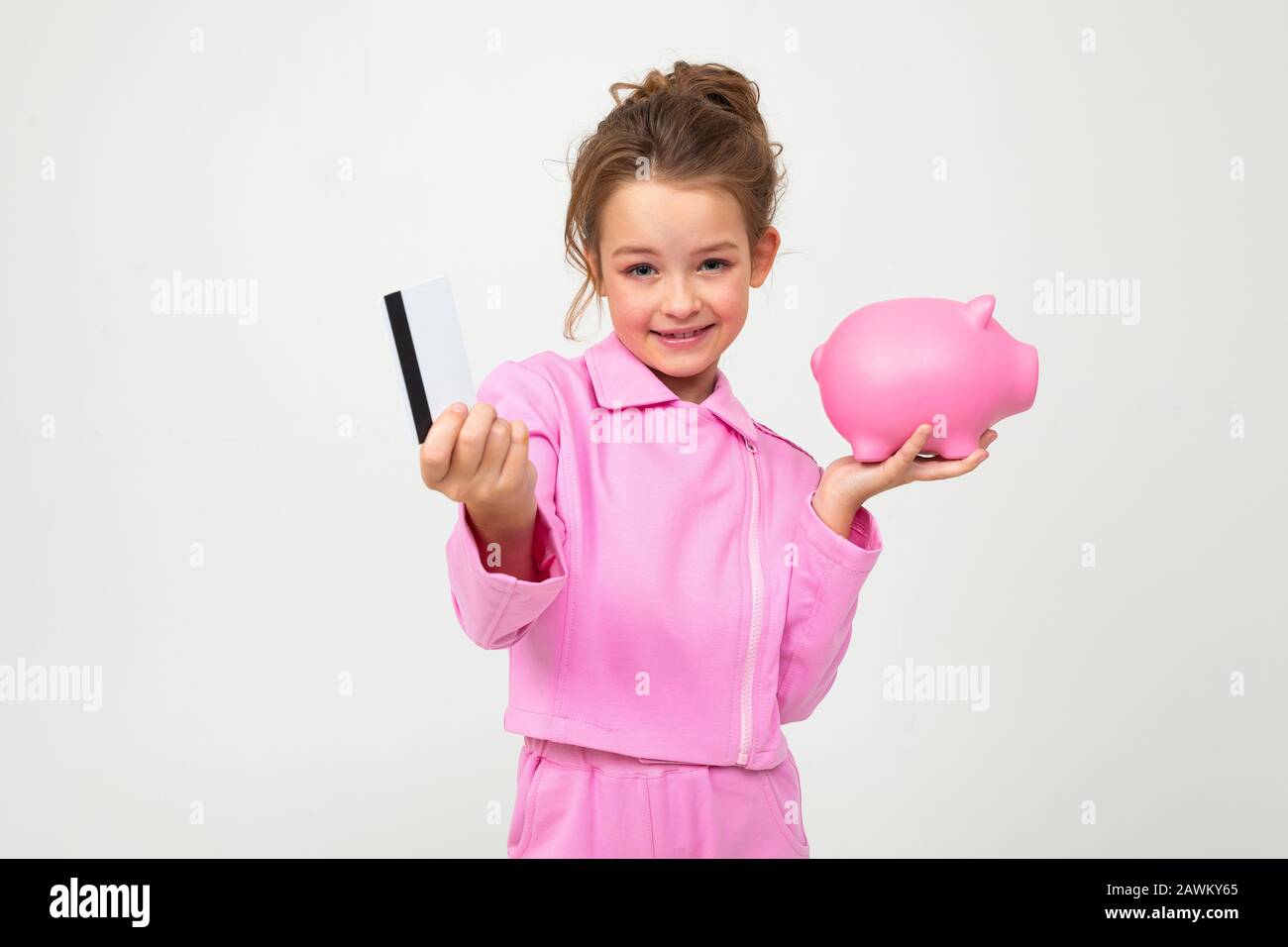 portrait of a beautiful young girl in a pink suit holding a piggy bank ...