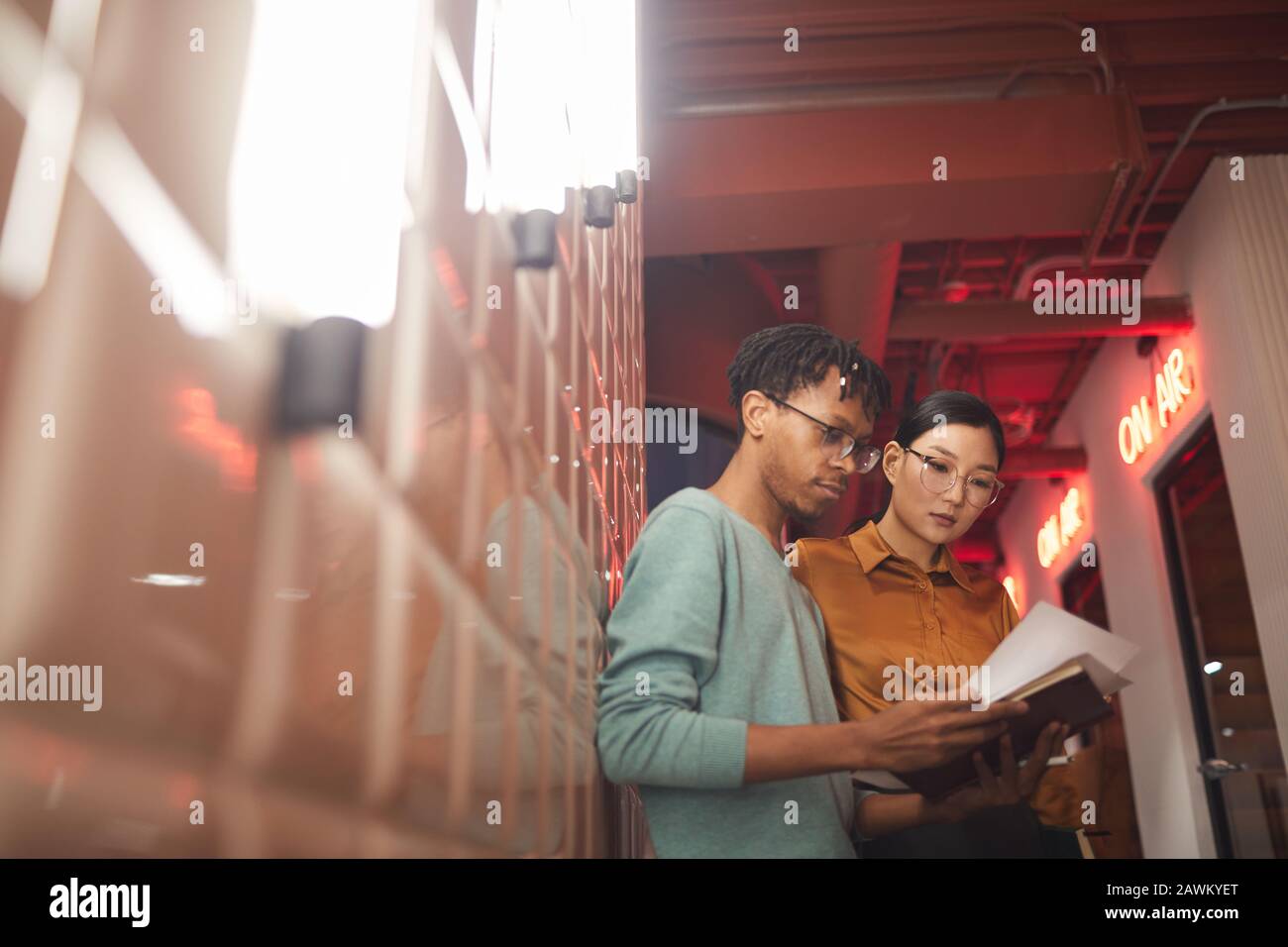 Waist up portrait of two ethnic business people discussing work documents while standing by wall outdoors in dim lighting, copy space Stock Photo