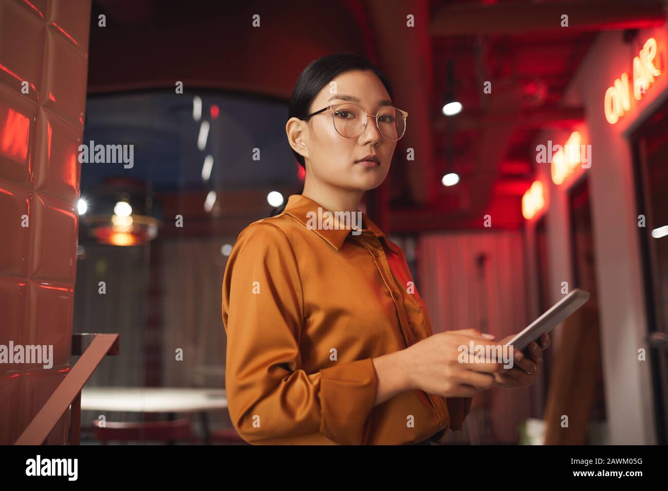 Waist up portrait of modern Asian businesswoman holding tablet and looking at camera while posing outdoors, copy space Stock Photo