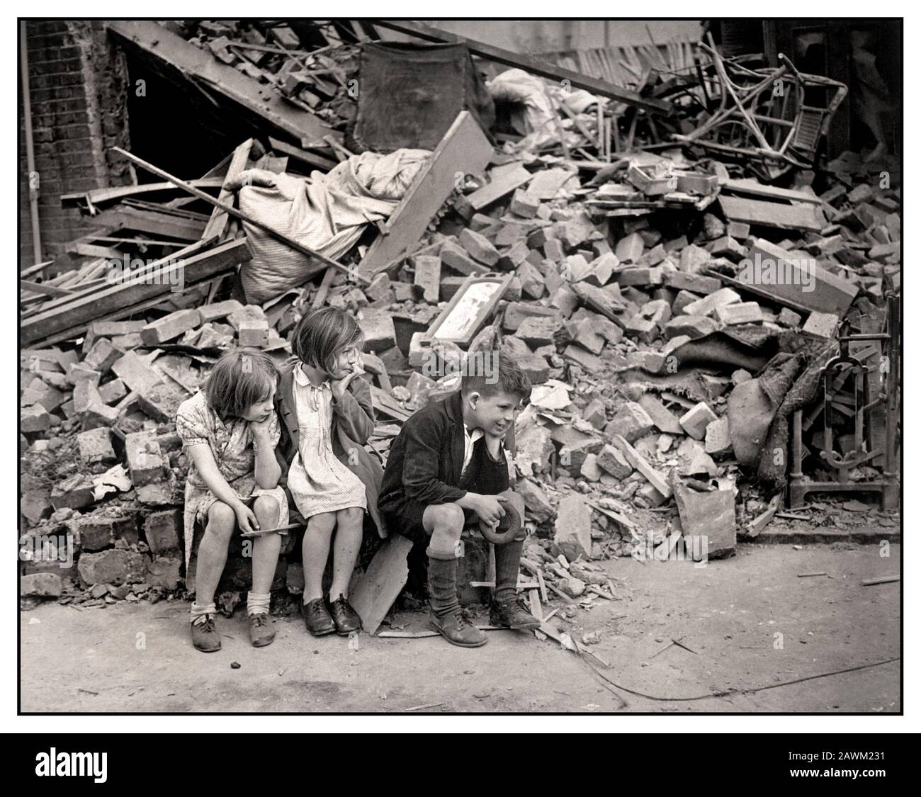 The London Blitz World War II 1940’s Children of East London, who have been made homeless by the random London Blitz bombs of Nazi Germany night bombing raids, waiting outside the wreckage of what was their home. September 1940. East London UK Stock Photo