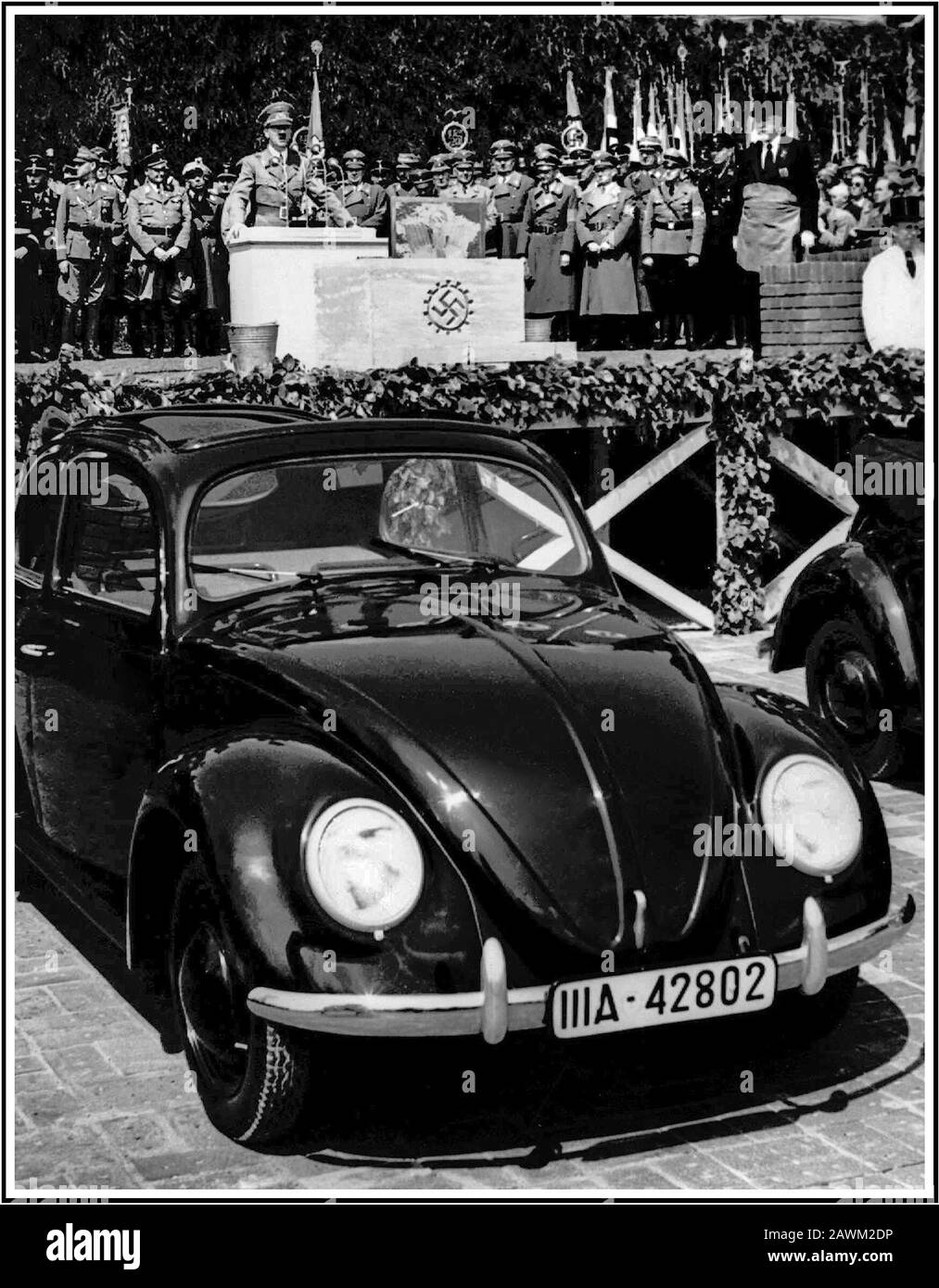 1930's ADOLF HITLER  SPEECH at KDF-Wagen VOLKSWAGEN launch. Hitler is making a speech behind the Nazi swastika engraved foundation stone at the launch of 'the people's car' KDF-Wagen VW Volkswagen Beetle air-cooled motorcar, an acclaimed and inspired design by the automotive genius Dr Porsche, launched at Fallersleben Wolfsburg Germany May 1938 Stock Photo