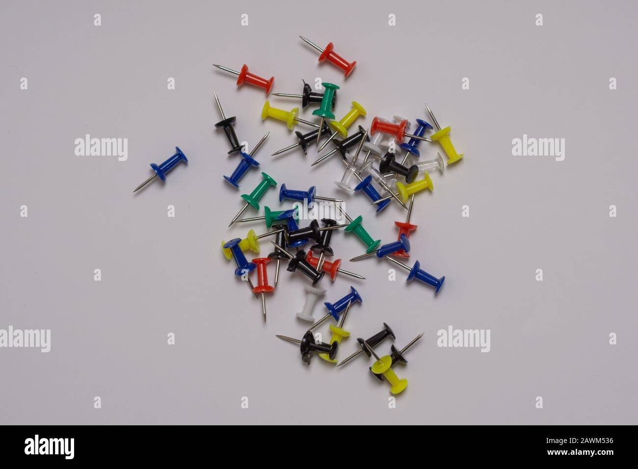 Thumbtacks of different bright colors are scattered randomly on a gray background Stock Photo