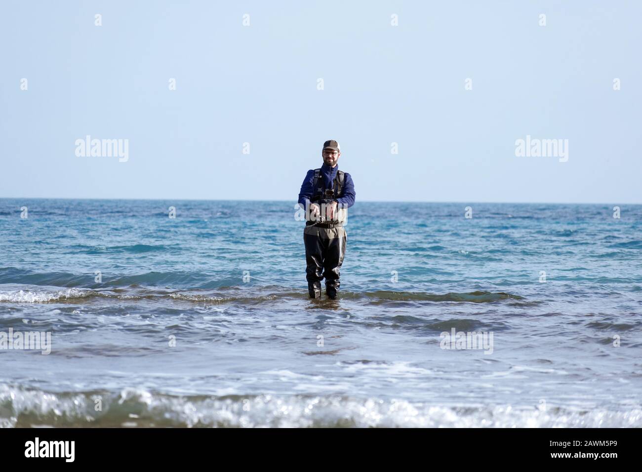 Fisherman standing at the seashore cast the fishimg rod. Sportsman holds a fishing rod and reel in a hooked fish. Spin Fishing hobby catching a fish a Stock Photo
