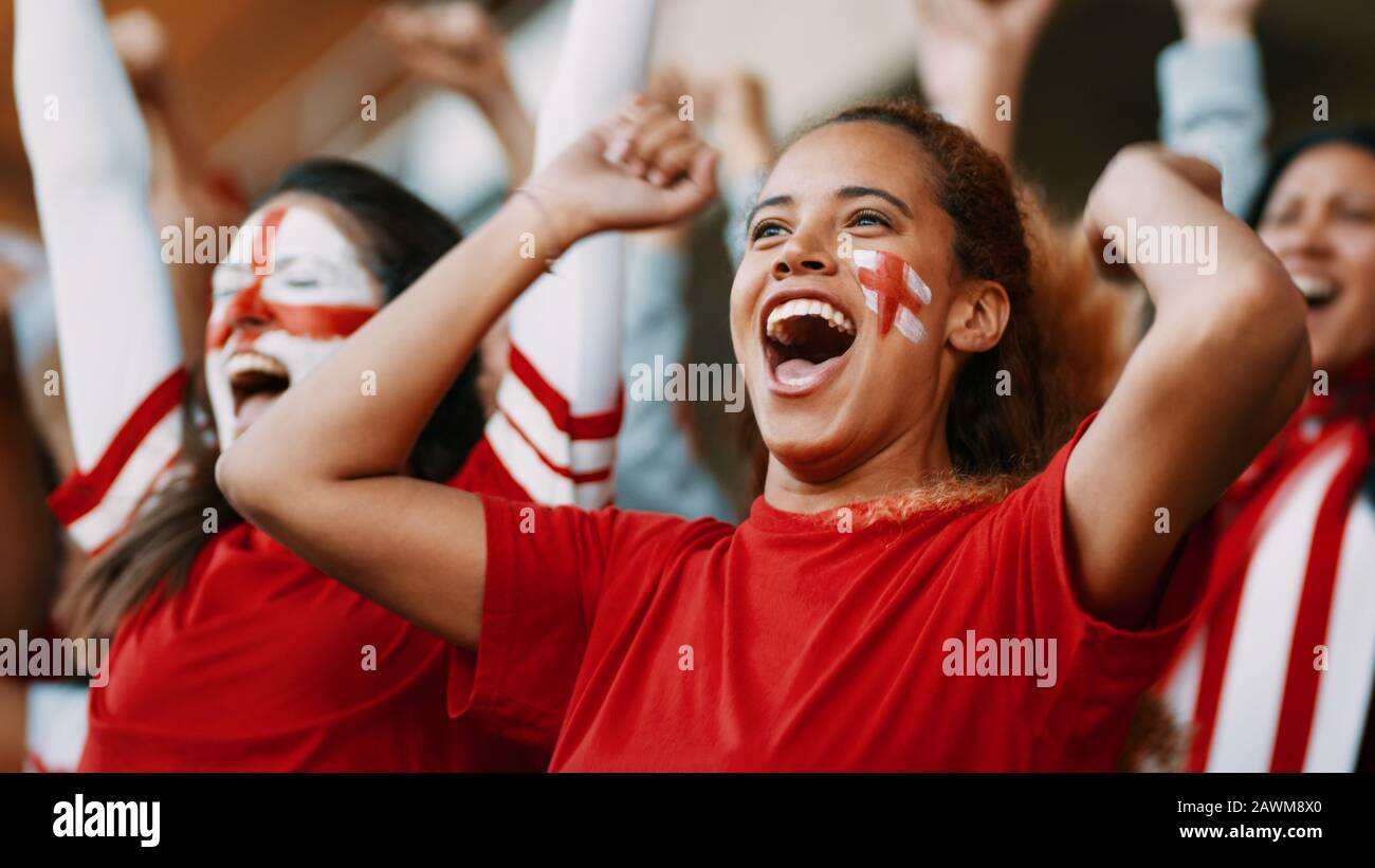 Female soccer fans of England watching and celebrating their team's victory. English female spectators enjoying after a win at stadium. Stock Photo