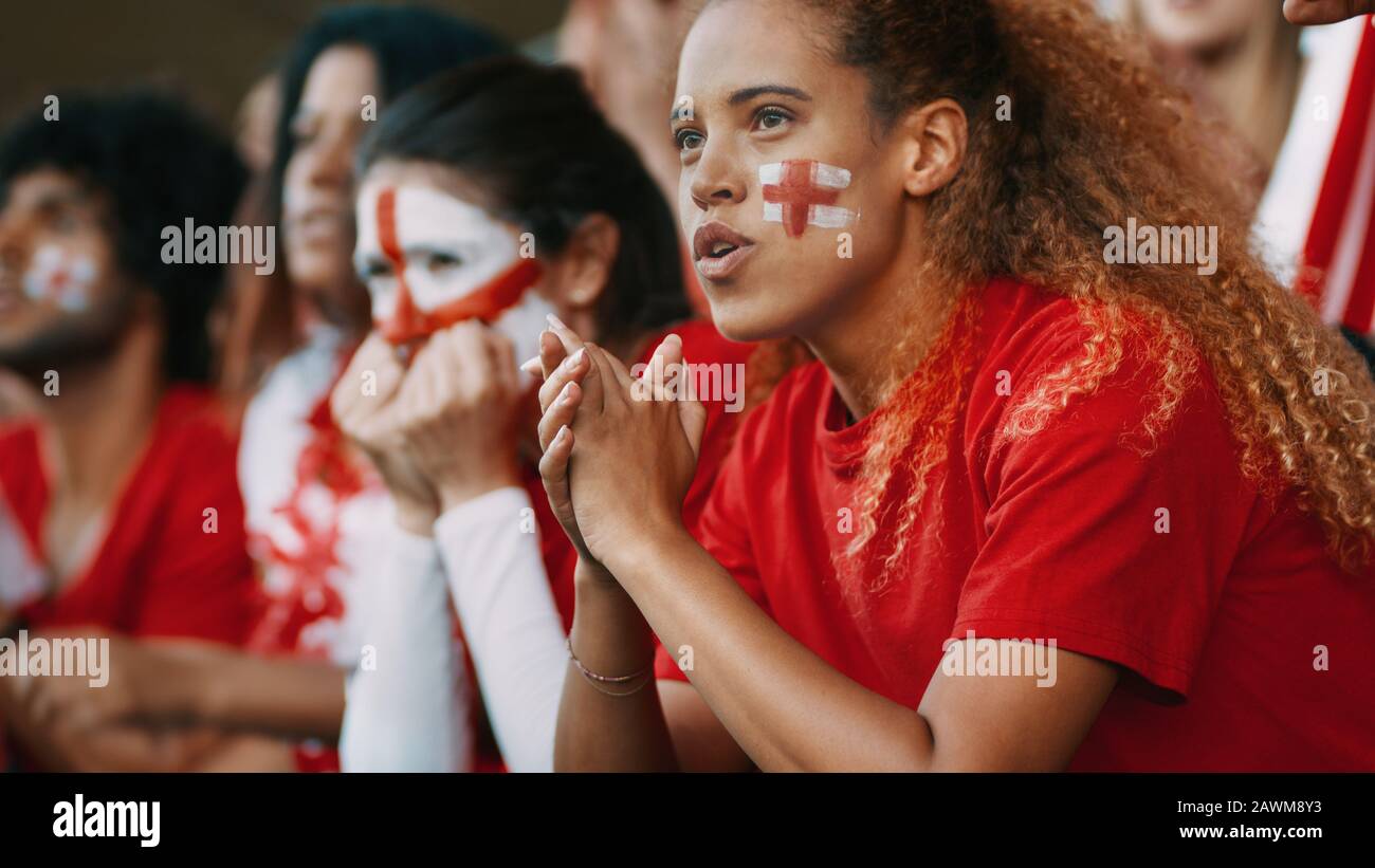 Anxious looking female soccer fans watching the game at stadium. Group of English football team supporters watching the match closely from the stands Stock Photo