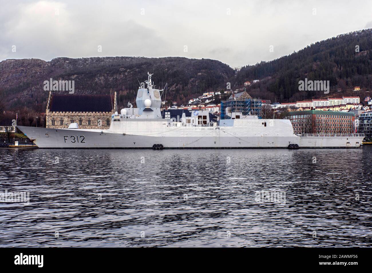 Norwegian warship, frigate F312 KNM Otto Sverdrup in front of ancient Haakonshallen.  Moored at Festningskaien quay in port of Bergen, Norway.  A dark Stock Photo