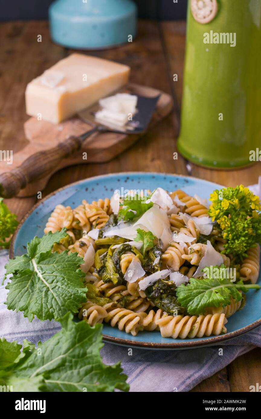 Cime di rapa pasta in a plate on with parmesan on a wooden table. Traditional food of the south of Italy, from Puglia. Rustic style photo. Copy space. Stock Photo