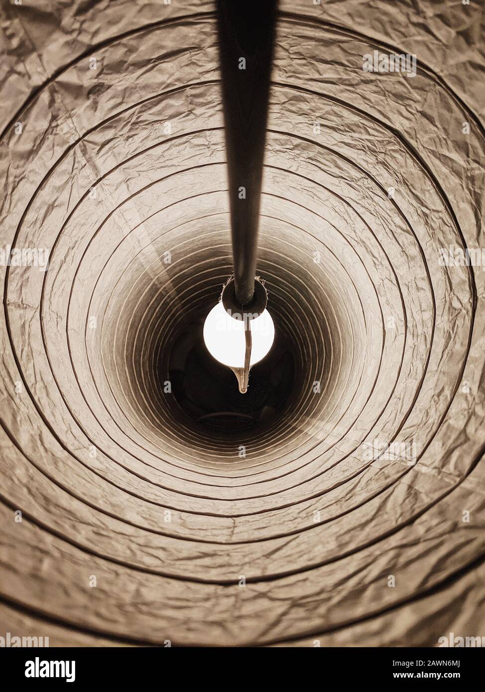 Inside of a lampshade with a white lightbulb turned on in a dark room