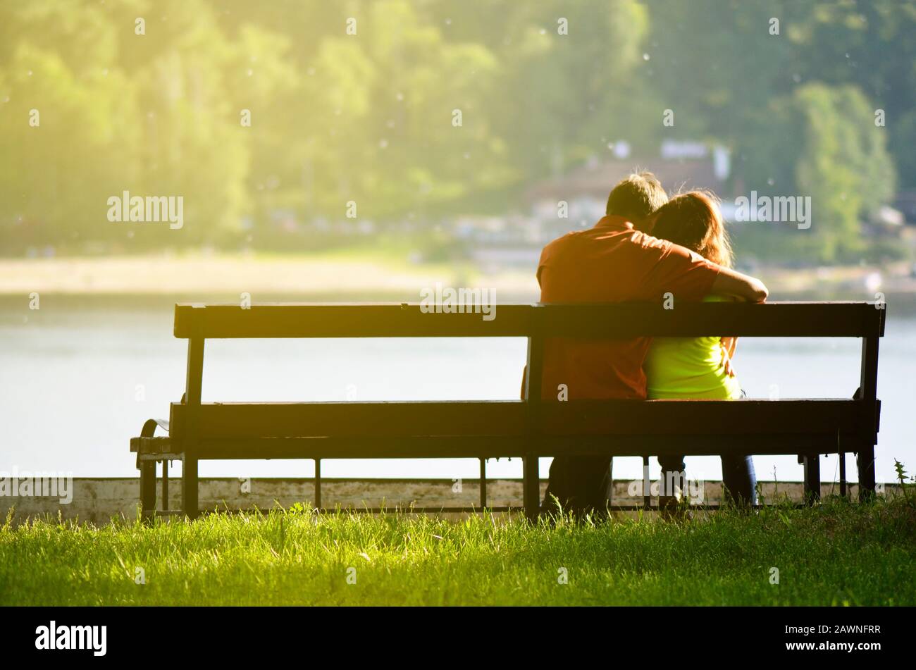 Rear view of a young couple sitting on a park bench. Romantic silhouette of people in love. Stock Photo