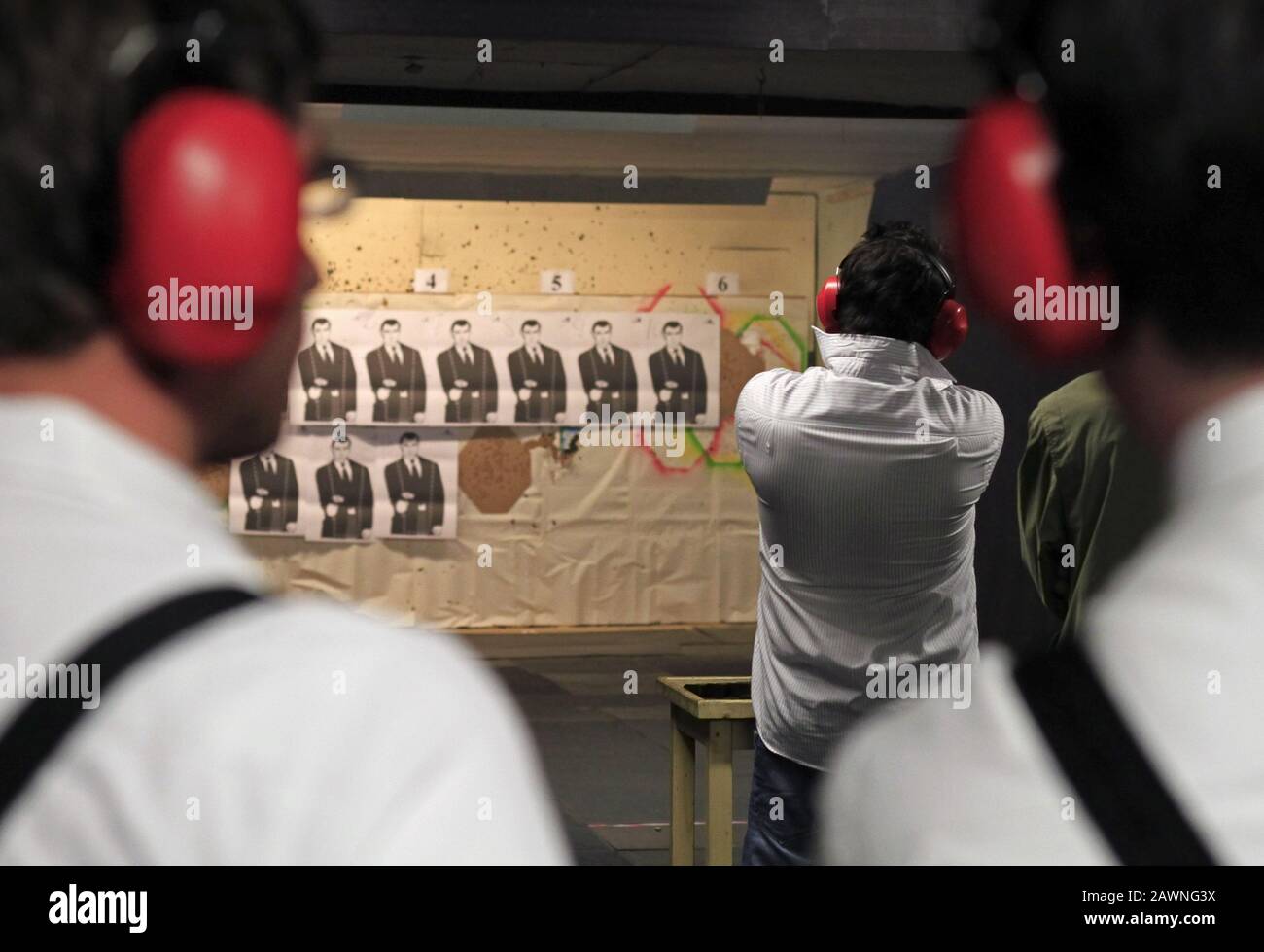 Man in red headphones shooting with shooting range seen from behind