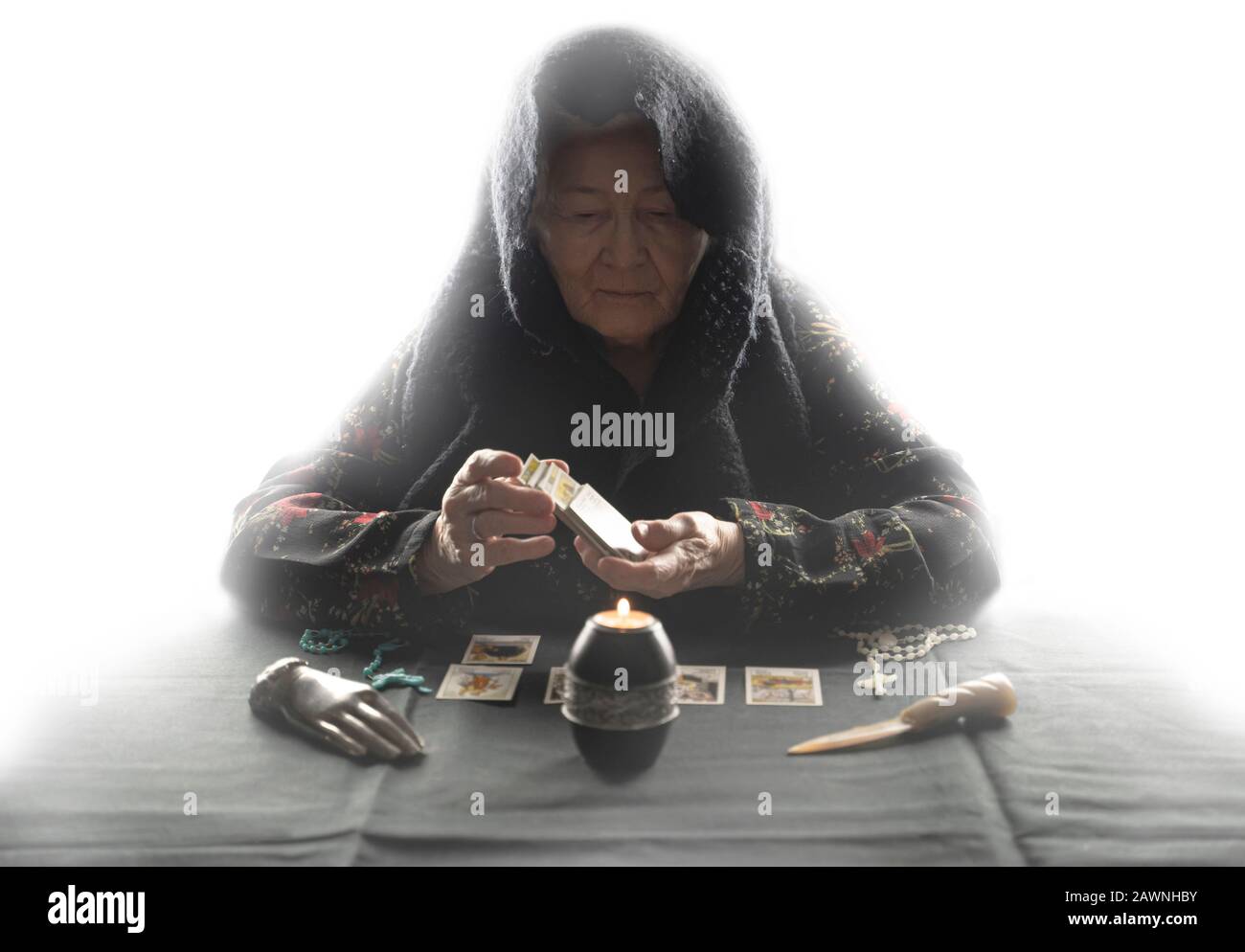 An old woman shuffle tarot cards above other tarot cards. Old wrinkeld hands. Occult fortune telling concept. White mystical background. Stock Photo