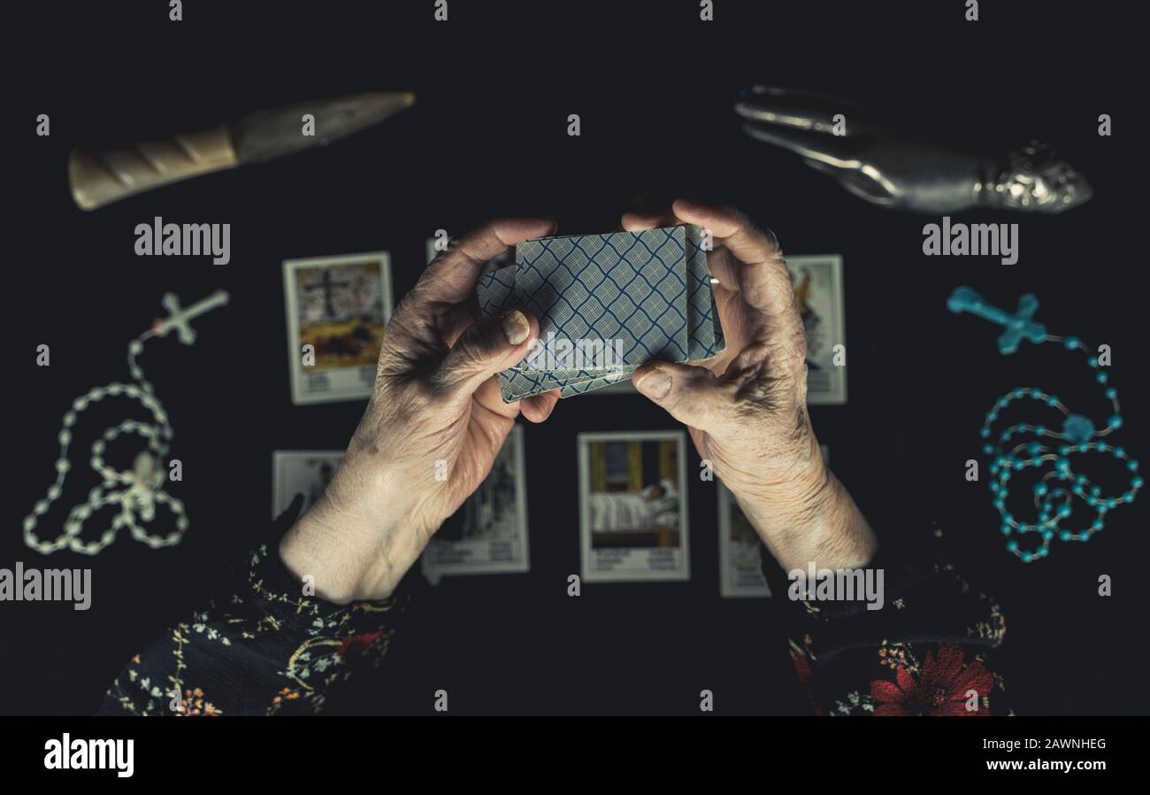 Old woman shuffle tarot cards above other tarot cards. Old wrinkeld hands. Occult fortune telling concept. Picture taken from above. Stock Photo