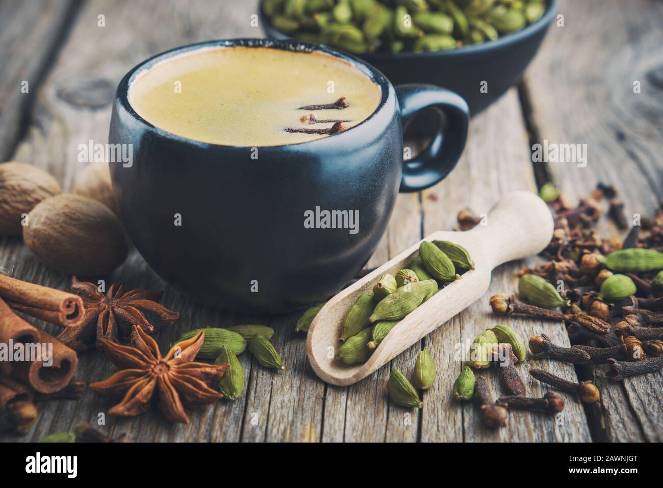 Cup of healthy ayurvedic masala tea or coffee with aromatic spices. Cinnamon sticks, cardamom, allspices and anise on wooden table. Stock Photo