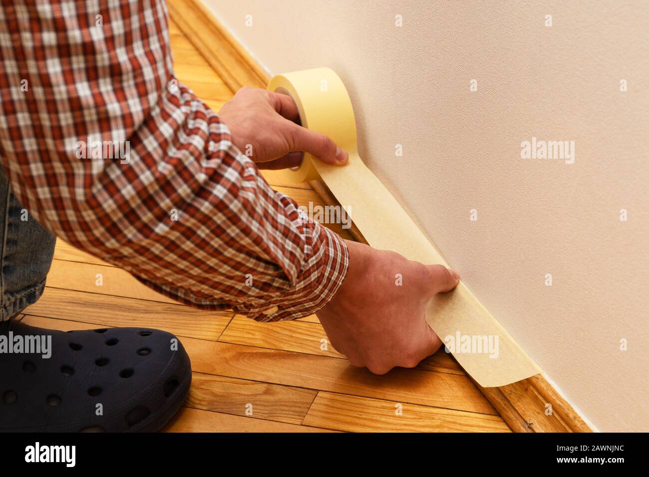 House Painter glues masking tape to the baseboard to protect it from