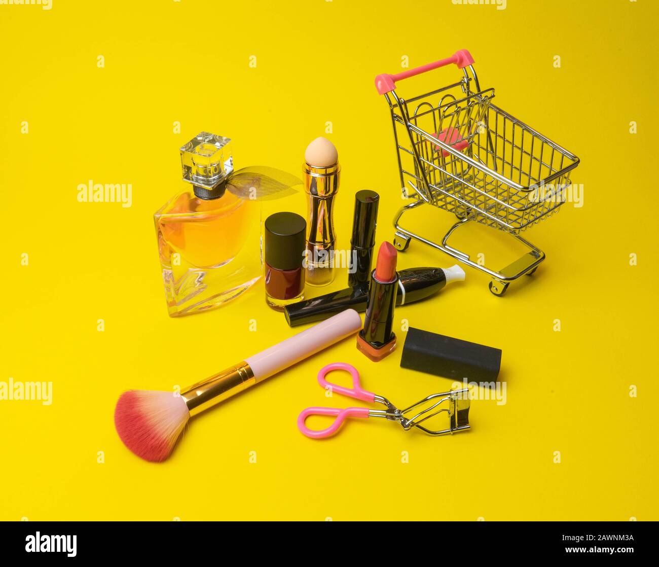 Makeup products fondant, mascara, perfume, brush, with cosmetic bag shopping cart on yellow background c Stock Photo
