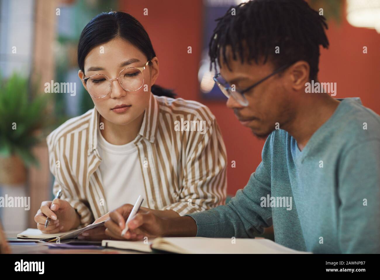 Portrait of two ethnic young people working on study project together while sitting at table in cafe Stock Photo