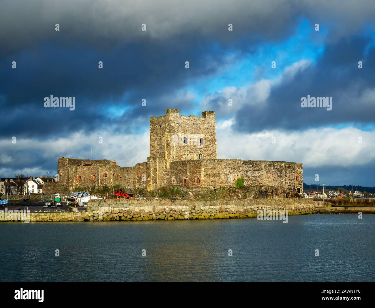 Medieval Norman Castle in Carrickfergus near Belfast, Northern Ireland, with marina in winter. Dramatic sky with dark stormy clouds. Sunset light Stock Photo