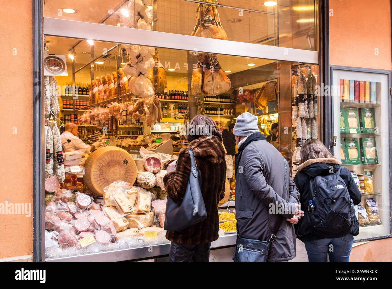 Bologna, Italy - December 2019: People looking at shop window with typical Italian food in Via Pescherie Vecchie, a famous alley full of traditional s Stock Photo