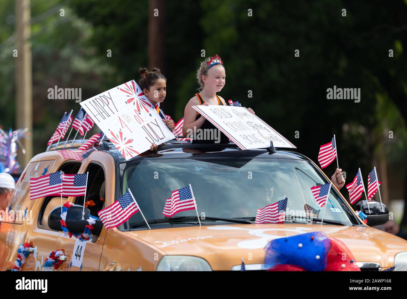 Arlington, Texas, USA - July 4, 2019: Arlington 4th of July Parade, Girls on a car with flags, holding signs that say Happy 4th of July Stock Photo